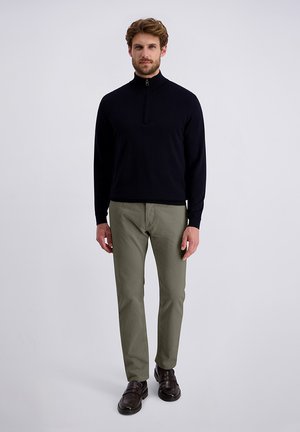 Pull zippé marine, pantalon vert clair, chaussures foncées. Le pull comporte un col montant ; le pantalon a une finition texturée. Design simple, couleurs neutres.