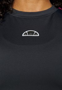 Camiseta atlética negra con un diseño de logo redondo y semitransparente en blanco y gris en el escote. Tejido suave y texturizado.