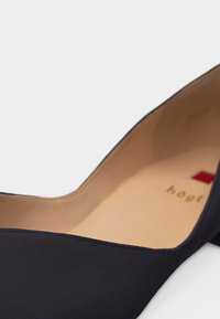 Chaussure noire à talon haut avec bout pointu, doublure intérieure beige et logo carré rouge visible à l'intérieur.