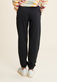 Pantalones de chándal negros con cintura y puños elásticos, con un tejido suave y ligero. Combinados con zapatillas blancas.