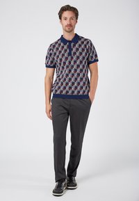 Kurzarm-Poloshirt in marineblau, rot und grauem geometrischem Muster. Gestrickter Kragen und Säume, kombiniert mit grauen Hosen und schwarzen Sneakern.