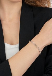 Silver chain bracelet with elongated links, featuring a polished finish, worn on a bare wrist, set against a dark blazer.