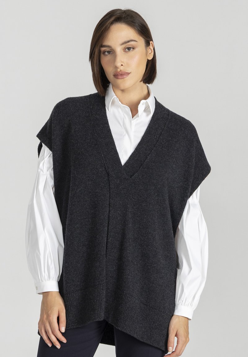 Ciemnoszara, dziana kamizelka z dekoltem w serek, krótkimi rękawami i luźnym krojem, noszona na białej koszuli z guzikami. Teksturowany materiał i ściągacz na dole.