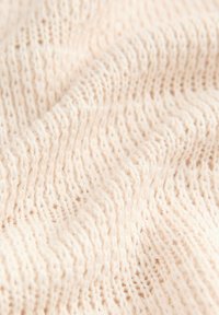 Cremfarbener, gestrickter Stoff mit einem strukturierten, offenen Webmuster. Weich, mit einer leicht elastischen Qualität, aus leichtem Garn gefertigt.