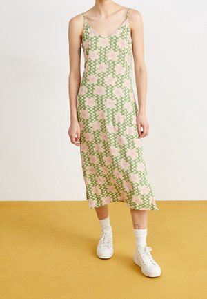 Sukienka midi bez rękawów w zielonym materiale z różowym wzorem kwiatowym i zygzakowatym. Dekolt w serek i boczne rozcięcia. Połączona z białymi trampkami i skarpetkami.