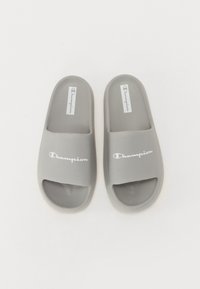 Grå glidelsandaler laget av syntetisk materiale. Har en åpen tå-design med en bred stropp og "Champion"-logo i hvitt. Myk tekstur.