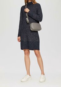 Vestido de punto en un azul marino oscuro con un cuello alto y textura acanalada, combinado con un bolso gris de bandolera y zapatillas blancas.