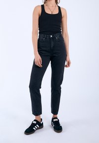 Svart hög midja jeans med rak bendesign. Bärs med en svart ribbad linne och gröna mockaskor med vita ränder.