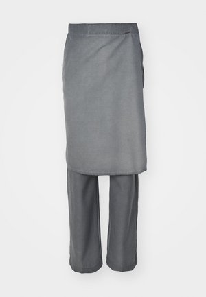Šedý dvoudílný outfit tvořený dlouhým topem s rovnými liniemi a volnými kalhotami, obě vyrobené z měkké látky s minimální texturou.