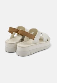 White platform sandals with a brown strap; smooth leather upper, open-back design, cushioned footbed, and textured rubber sole.