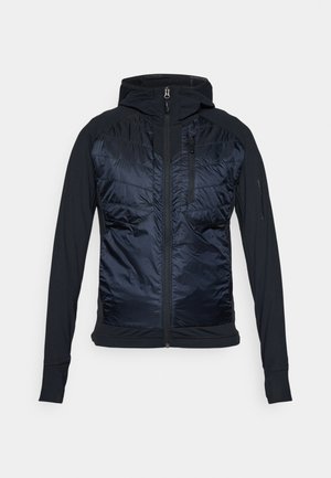 Veste hybride avec un devant en doudoune bleu marine foncé et des manches noires ajustées. Texture lisse, fermeture éclair à l'avant et capuche réglable.