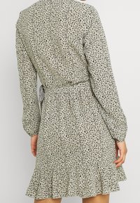 Robe verte à pois avec manches longues, un ourlet évasé et une ceinture à nouer à la taille. Le tissu est léger avec une texture douce.