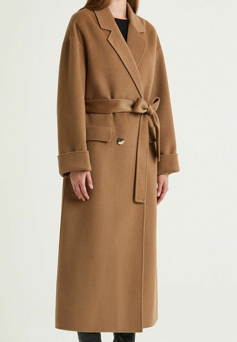 Cappotto in misto lana marrone con maniche lunghe, vita con cintura, colletto a revers, tasche applicate e silhouette dritta. Caratterizzato da un dettaglio con un singolo bottone.