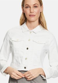 Witte, korte denimjas met lange mouwen, klassieke kraag, sluiting met knopen aan de voorkant en twee borstzakken met metalen accenten.