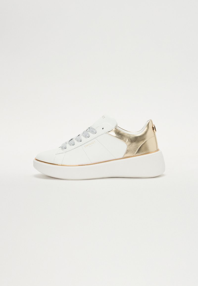 Fehér sneaker fémes arany kiegészítőkkel, bőrből készült, kerek forma, lapos talp, lapos ezüst fűzők, és logó részlet az oldalon.