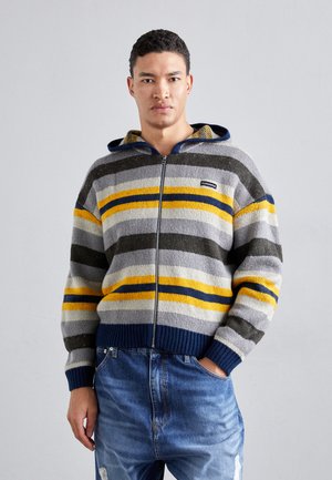Zipperowany sweter z kapturem w paski w odcieniach szarości, granatu, żółci i ciemnej zieleni. Dziani wzór z ściągaczami przy mankietach i kołnierzu. Luźny krój.