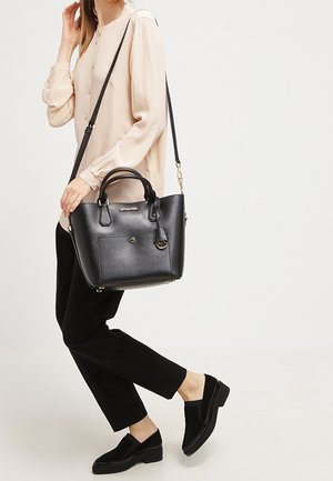 Sac à main en cuir noir avec double anses supérieures, bandoulière ajustable et petite poche avant. Assorti à un pantalon noir et des chaussures.
