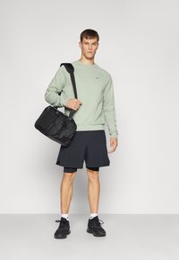Felpa verde chiaro, pantaloni corti sportivi neri, sneakers nere e una borsa a spalla nera. Design semplice, con branding minimal sulla felpa.