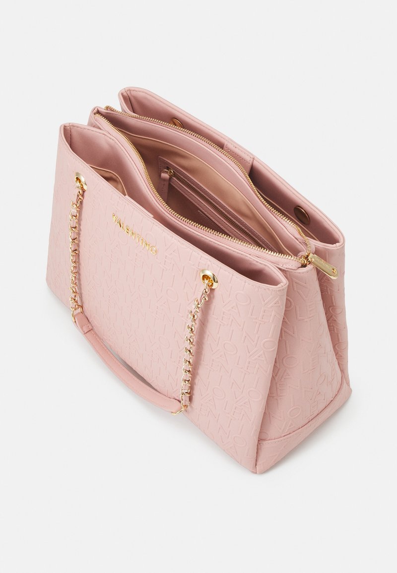 Sac à main rose clair en matériau texturé avec quincaillerie dorée, doté d'une bandoulière en chaîne et de plusieurs compartiments à l'intérieur.