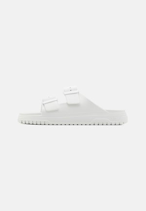 Witte rubberen slidersandalen met twee verstelbare banden en een gestructureerd oppervlak. Beschikt over een robuuste zool met horizontale groeven voor grip.