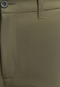 Olijf groene stoffen broek met een gladde textuur, een voorzak en een knoopsluiting. De stiksels zijn fijn en subtiel.
