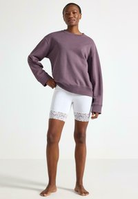 Lilla sweatshirt med lange ærmer og afslappet pasform kombineret med hvide shorts med dekorativ blonderkant ved kanten.