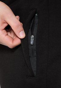 Schwarze Reißverschlusstasche aus elastischem Stoff, die eine Hand zeigt, die den Reißverschluss greift. Glatte Textur mit eleganten Designdetails.