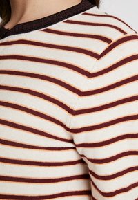 Gestreifter Pullover in Creme, Weinrot und hellem Pfirsich, mit rundem, dunklem Rippenkragen und weicher Strickstruktur, versehen mit schrägen Streifen.