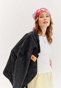 Czarna dżinsowa kurtka z kolorową naszywką, biała dopasowana koszulka i żywy kwiatowy szalik. Wyraźne tekstury i swobodny krój.