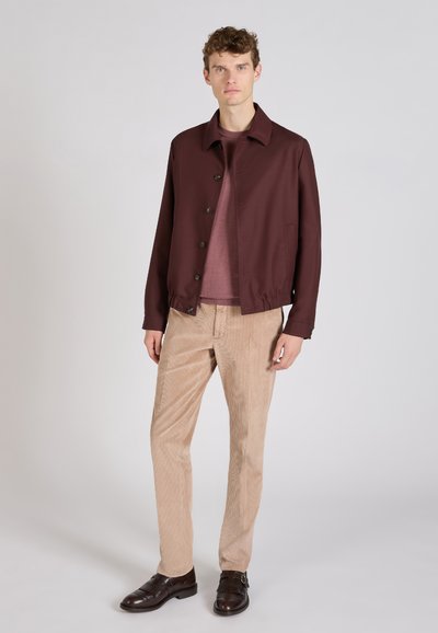 Burgundowa lekka kurtka z guzikami z przodu, zestawiona z różowym topem i beżowymi spodniami z kordurowej tkaniny. Brązowe buty dopełniają stylizację.