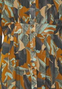 Gros plan d'une robe avec un motif abstrait de feuilles orange, beige, verte et noire, rayures verticales, fermeture à boutons et ceinture assortie à la taille.