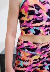 Tenue de fitness colorée comprenant un haut court et des leggings dans des nuances vibrantes de rose, orange et noir avec des motifs abstraits. Tissu doux et extensible.