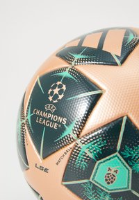 Svart och kopparfärgad fotboll med texturerad yta, som har en Champions League-logotyp och stjärnmönster, märkt "MATCHBALL" och "REPLICA".