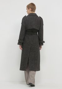 Cappotto lungo, grigio scuro, con texture, vita aderente, design con cintura e collo oversize; presenta maniche con risvolto e uno spacco posteriore.