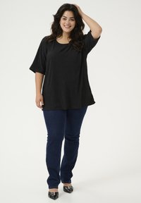 Haut noir texturé à manches courtes associé à un jean slim bleu foncé et des chaussures noires pointues avec des accents décoratifs.