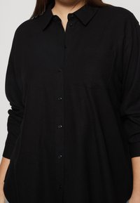 Schwarze Hemdbluse aus einem glatten Stoff, mit Kragen, langen Ärmeln, einer Brusttasche und vorderen Knopfverschlüssen.