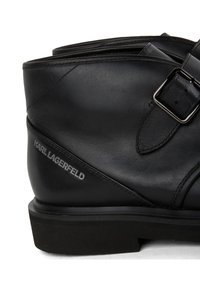 Black leather ankle boot with a flat sole, featuring a buckle detail and embossed "KARL LAGERFELD" logo on the side. Smooth texture.