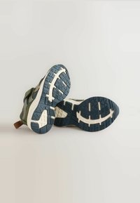 Sportowe buty w zielono-szarej siateczce z ciemnoniebieskimi gumowymi podeszwami. Grube bieżniki i brązowa pętla przy pięcie ułatwiająca zakładanie.