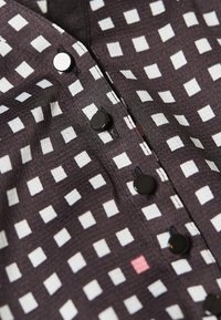 Nära bild av svart tyg med vitt rutmönster, som visar fyra svarta knappar och en vit knapp längs sömmen.