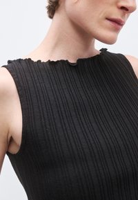 Μαύρο αμάνικο τοπ με ριμπ υφή, μπούστο με βολάν και εφαρμοστή γραμμή, που τονίζει τις καθαρές γραμμές και την απλότητα.