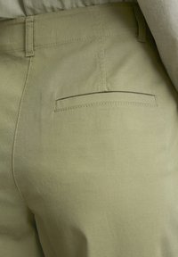 Light green, tailored trousers with a smooth texture and minimal detailing, featuring a back pocket with a straight, stitched opening.