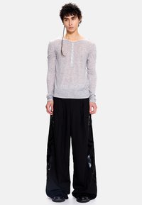 Ilgas rankovėmis šviesiai pilkas aptemptas marškinėlis su henley kaklu ir sagų detalėmis, derinamas su laisvomis juodomis kelnėmis, puoštomis blizgančiais šonais.