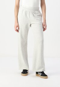 Light gray sweatpants made of soft fabric, featuring a wide-leg design and an elastic waistband. Paired with black shoes and a white top.