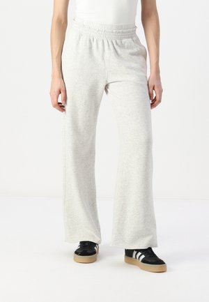 Helle graue Jogginghose aus weichem Stoff, mit einem weiten Bein und einem elastischen Bund. Kombiniert mit schwarzen Schuhen und einem weißen Oberteil.