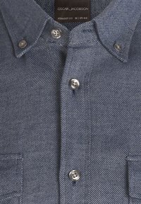 Camicia in denim blu scuro con un motivo a strisce testurizzate. Presenta un colletto con bottoni e bottoni argentati. Include un dettaglio con taschino sul petto.