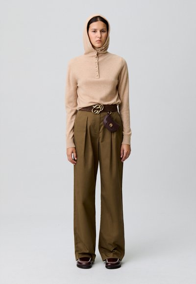 Pull en tricot beige avec capuche et patte de boutonnage, associé à un pantalon ample vert olive et une ceinture marron avec une petite pochette.