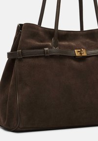 Brązowa zamszowa torebka z dwoma solidnymi uchwytami, ozdobiona dekoracyjnym skórzanym paskiem i złotym zapięciem. Gładka tekstura i uporządkowany kształt.