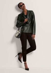 Groene leren blazer met notch-lapels, twee knopen, gecombineerd met zwarte broek en zwarte enkelsandalen. Accessoire: kleine handtas.