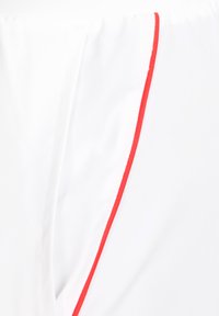 Shorts blancs avec une texture lisse, ornés d'une garniture rouge sur le côté, mettant en avant le design épuré et la coupe athlétique.