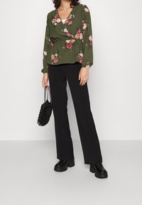 Zielona bluzka w kwiaty z zapięciem w stylu wrap oraz peplum w talii, połączona z czarnymi spodniami o szerokich nogawkach i masywnymi czarnymi butami na platformie. Czarna siatkowa torba.